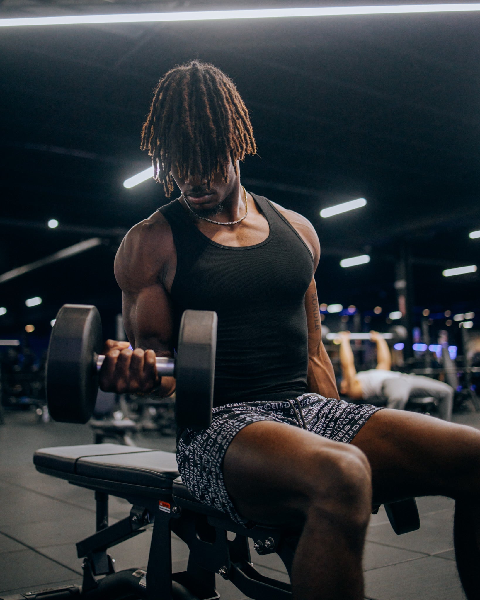 A bodybuilder working out at the gym wearing a premium fitted tank top in black and 4 inch inseam mesh shorts in black, from SquidHaus