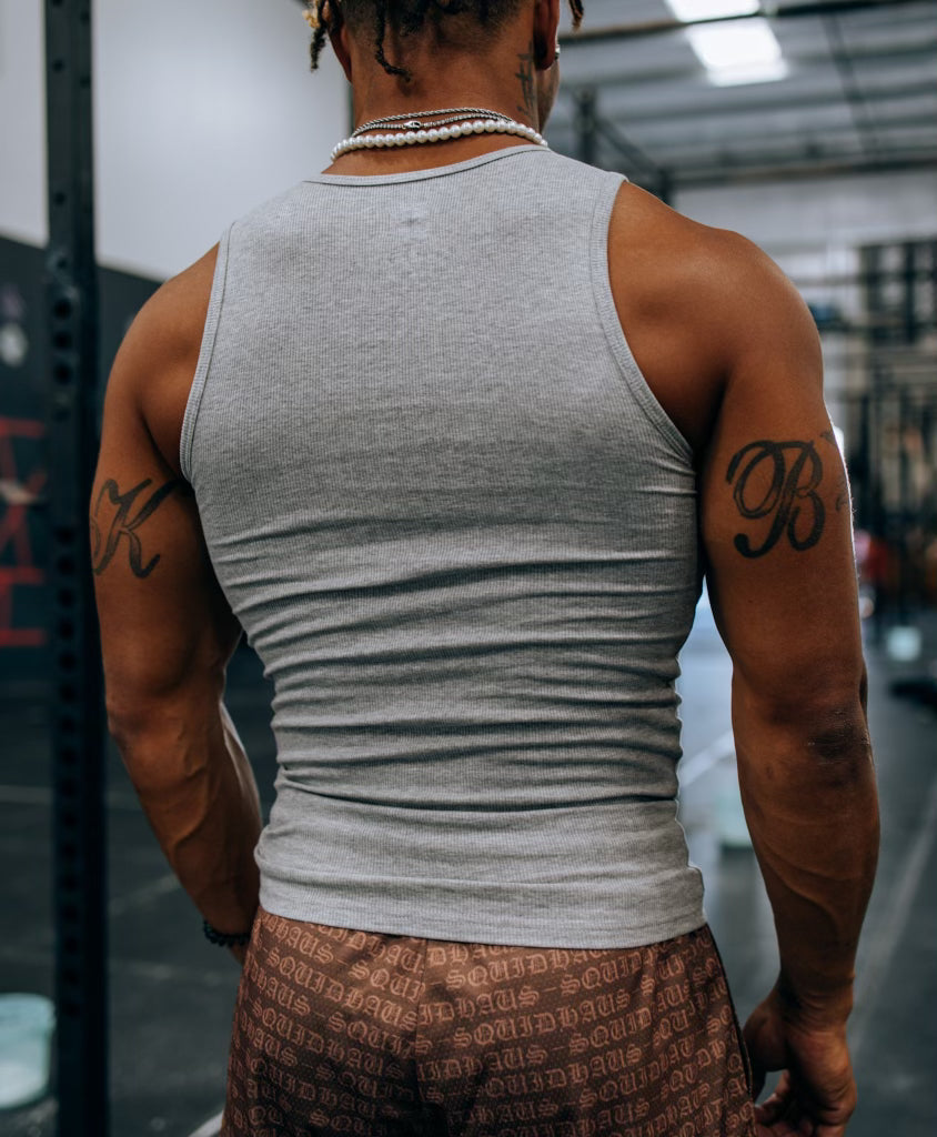 A rear view of a body builder at the gym wearing 4" inseam mesh shorts in brown, from SquidHaus