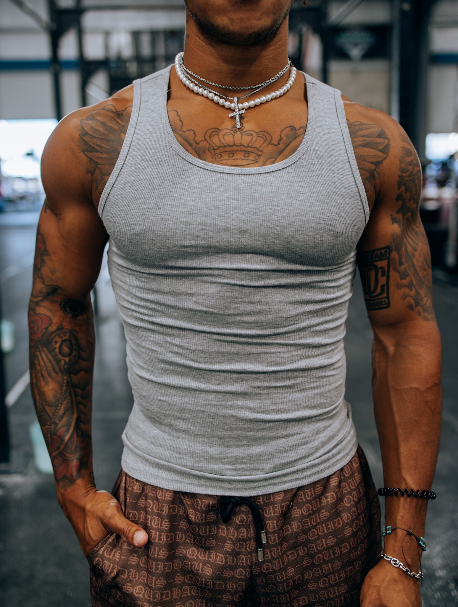 An athlete at the gym wearing a gray premium fitted tank top and 4" inseam mesh shorts in brown, both by SquidHaus