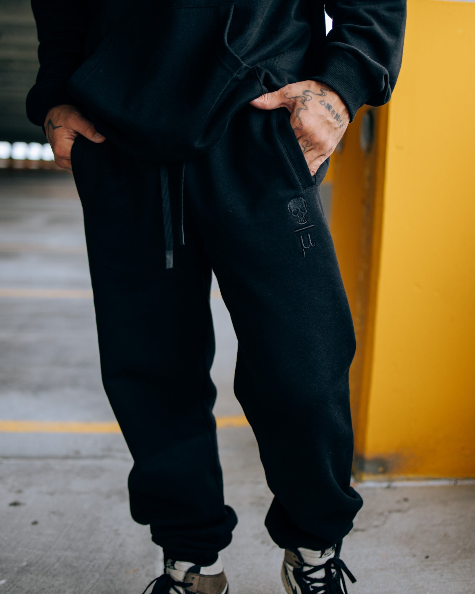 A man wearing Death Over Average sweatpants and the Lip Tat Hoodie by SquidHaus