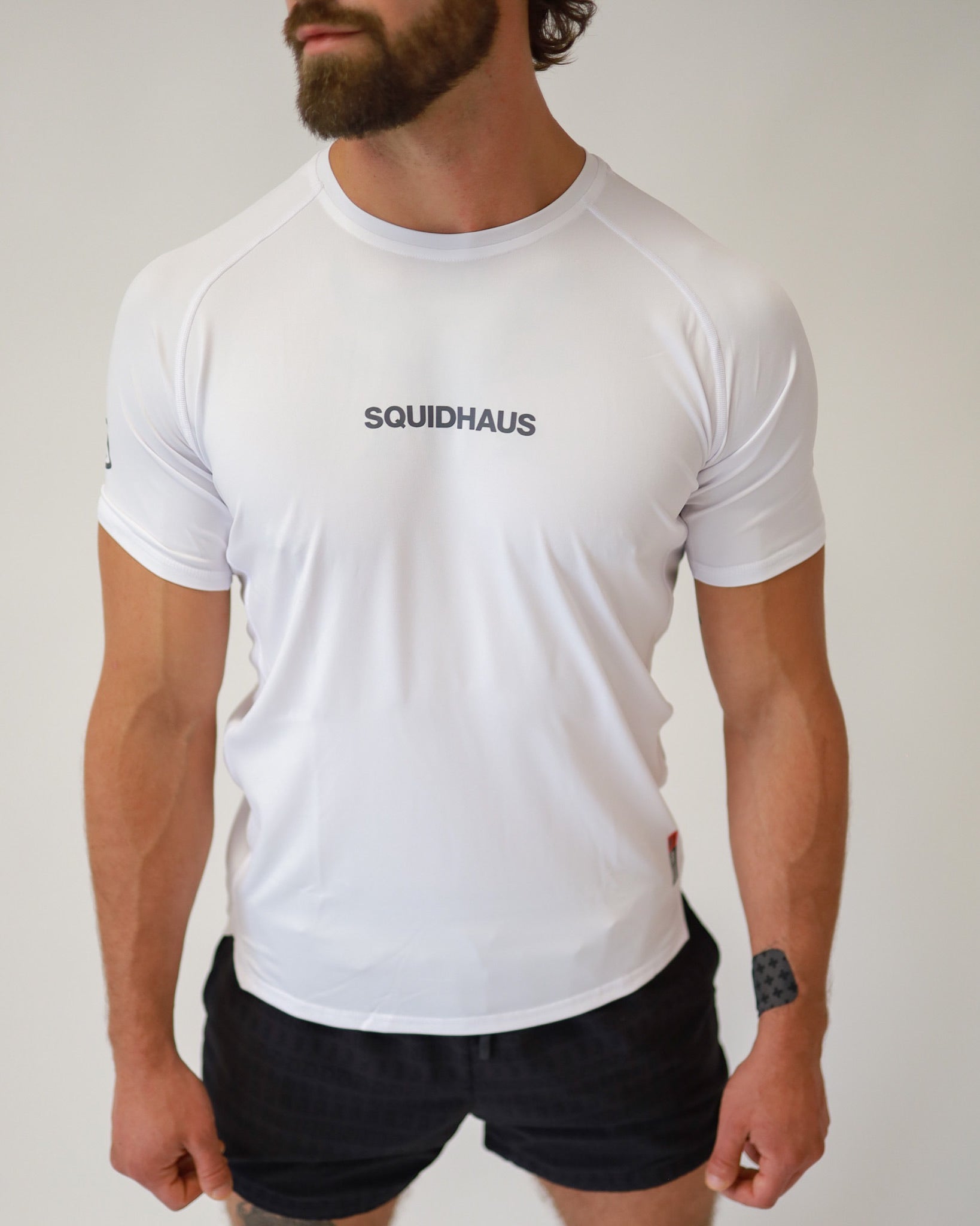 Front view of an athlete wearing a Pro-Tech V1 athletic fitted short sleeve t-shirt in white with 4" inseam mesh shorts in black, from SquidHaus