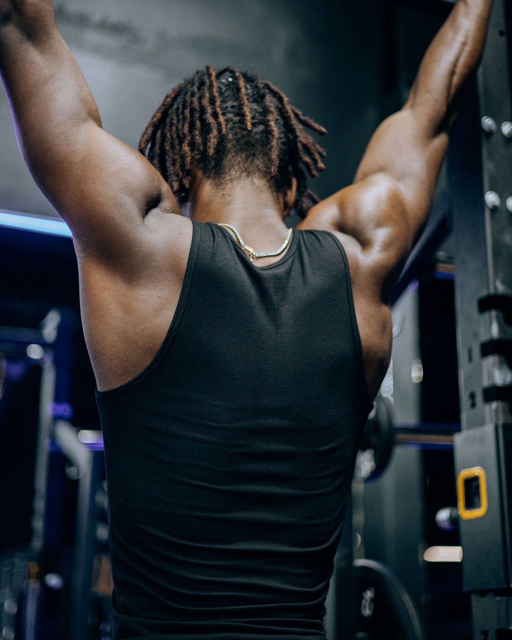 A bodybuilder working out at the gym wearing a premium fitted tank top in black from SquidHaus