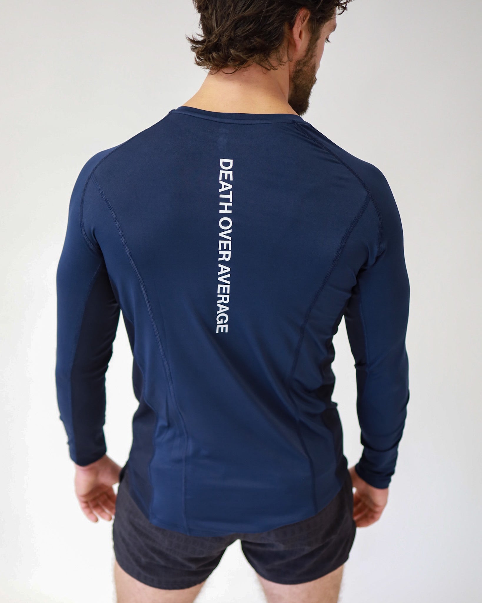 A rear view of an athlete wearing a Pro-Tech V1 athletic-fitted long sleeve t-shirt in navy blue and 4" inseam mesh shorts in black, both from SquidHaus