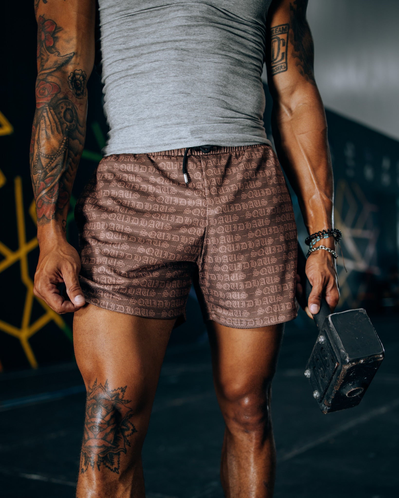 An athletic man at the gym wearing 4" inseam mesh shorts in brown with a gray premium fitted workout tank