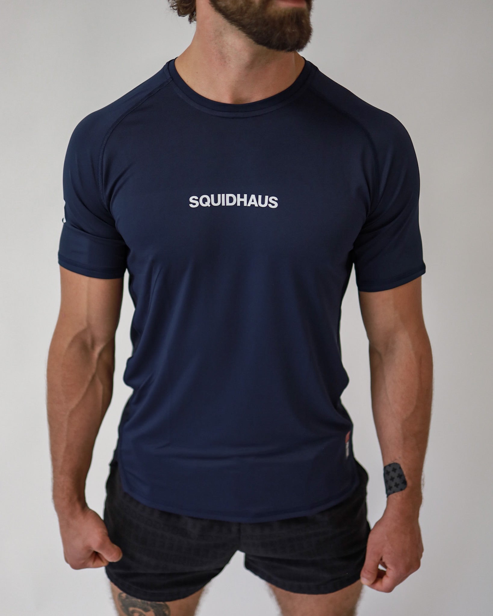 Front view of an athlete wearing a Pro-Tech V1 athletic fitted short sleeve t-shirt in navy blue with 4" inseam mesh shorts in black, from SquidHaus