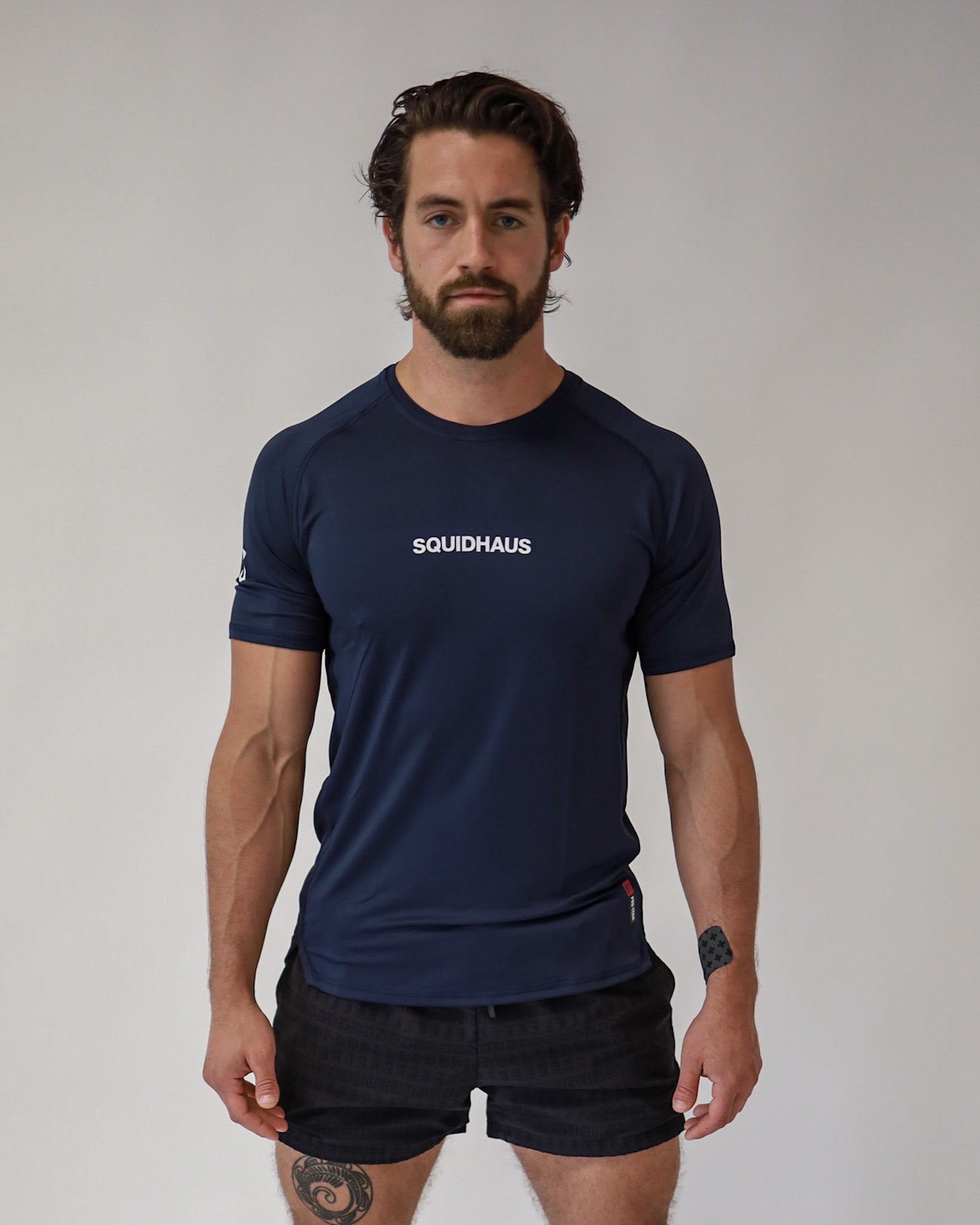 An athletic man wearing a Pro-Tech V1 athletic fitted short sleeve t-shirt in navy blue with 4" inseam mesh shorts in black, from SquidHaus