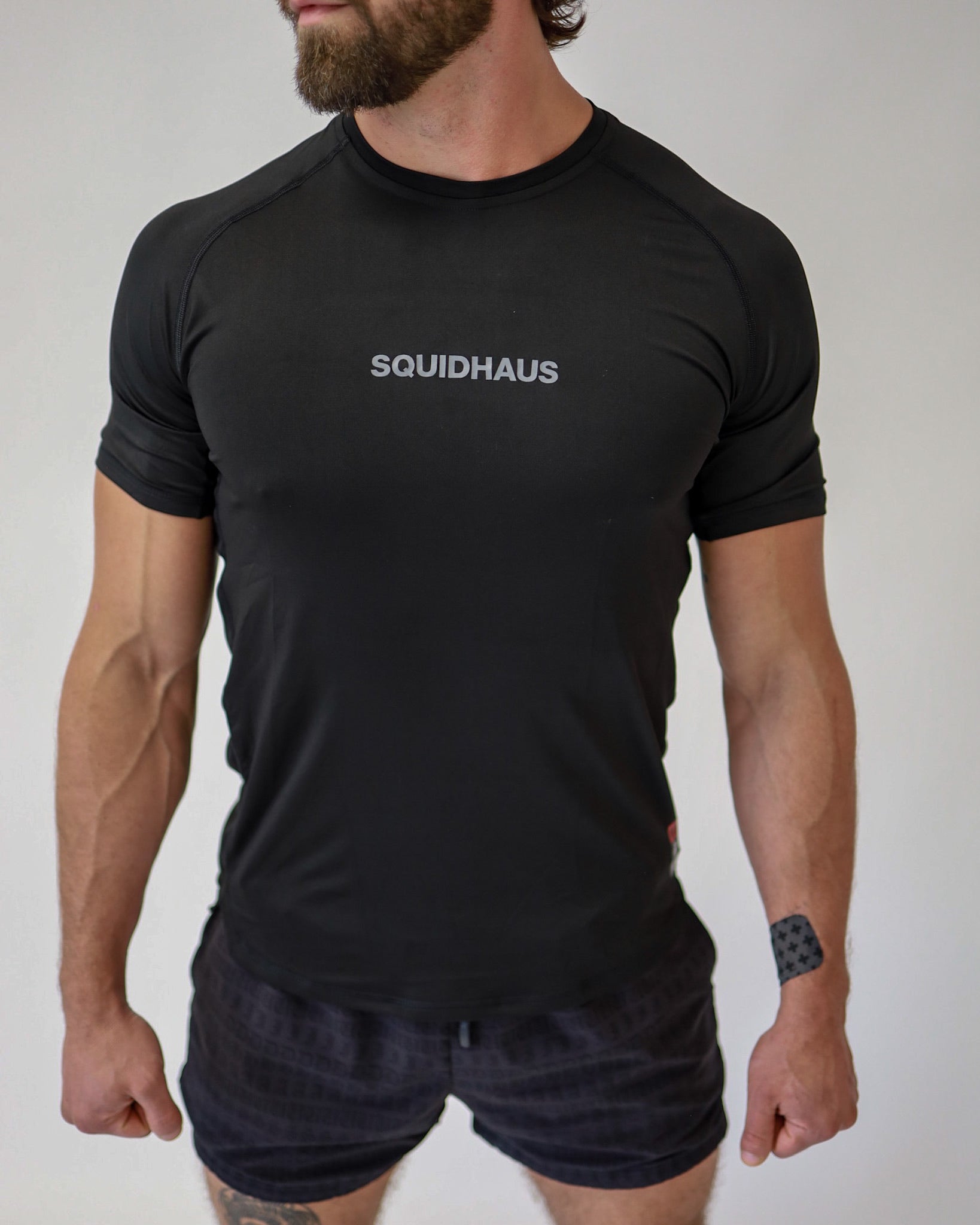 Front view of an athlete wearing a Pro-Tech V1 athletic fitted short sleeve t-shirt in black with 4" inseam mesh shorts, from SquidHaus