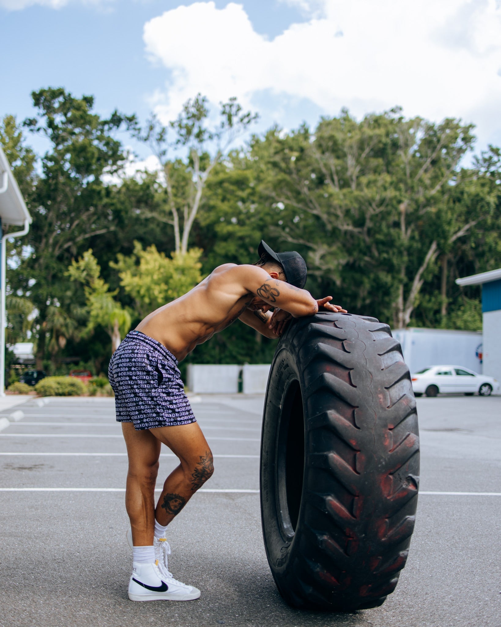 An athlete wearing 4 inch inseam mesh shorts in purple is taking a breather from working out with a large tire 