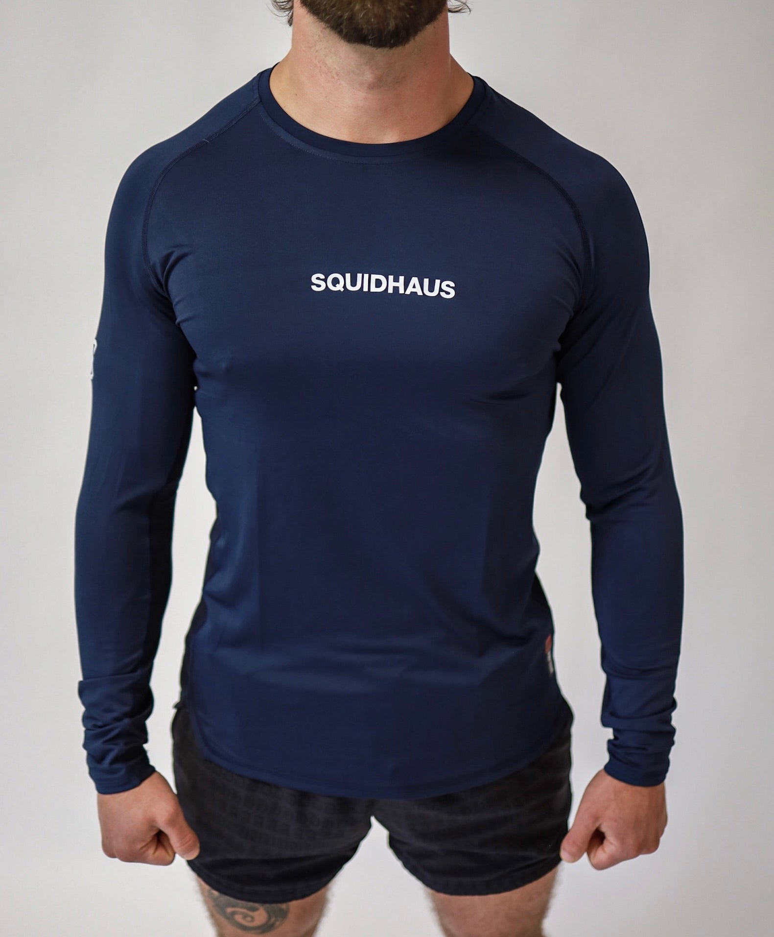 A front view of an athlete wearing a Pro-Tech V1 athletic-fitted long sleeve t-shirt in navy blue and 4" inseam mesh shorts in black, both from SquidHaus