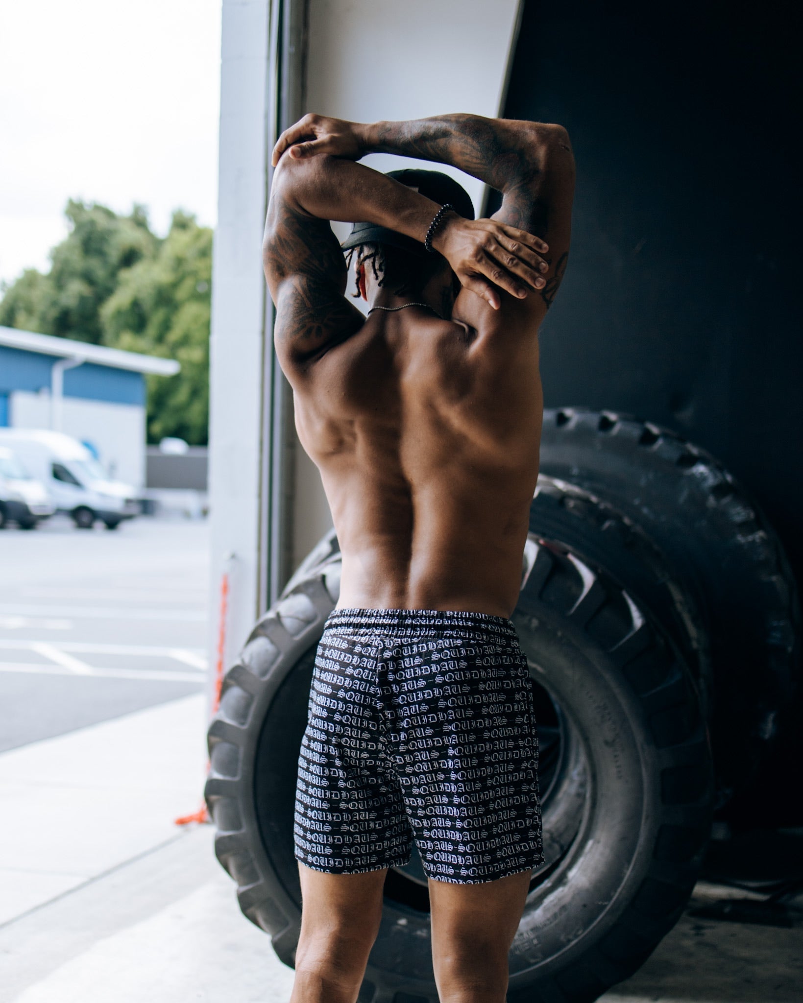 An athlete stretching in front of a workout tire while wearing 4 inch inseam mesh shorts in black from SquidHaus