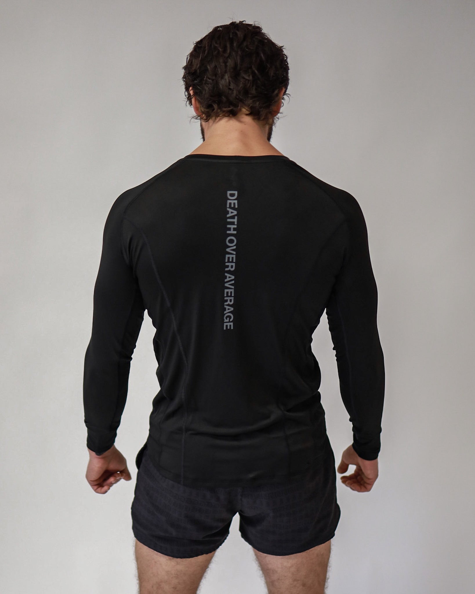 A rear view of an athlete wearing a Pro-Tech V1 athletic-fitted long sleeve t-shirt and 4" inseam mesh shorts in black, both from SquidHaus