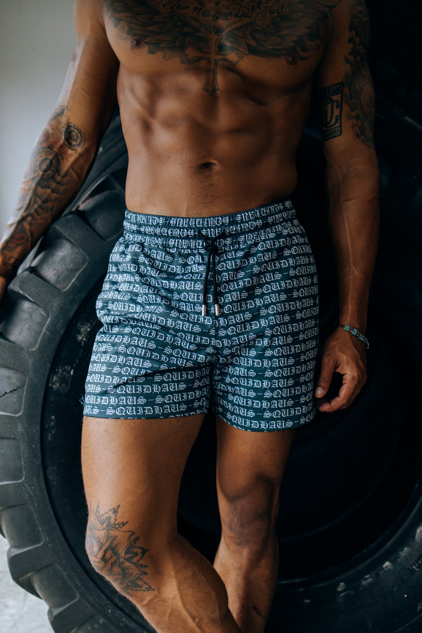 A bodybuilder posing in front of a large tire, wearing 4 inch inseam mesh shorts in green