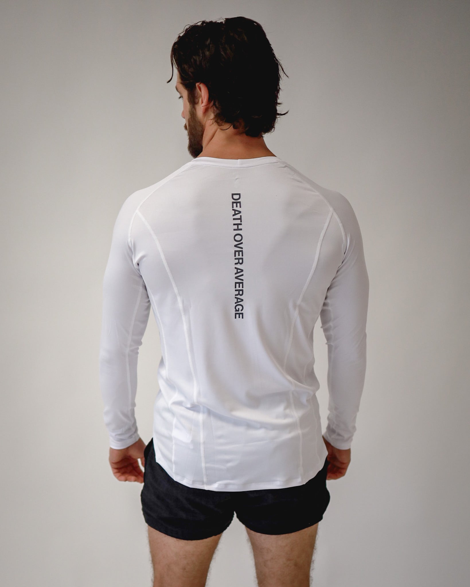 A rear view of an athlete wearing a Pro-Tech V1 athletic-fitted long sleeve t-shirt in white and 4" inseam mesh shorts in black, both from SquidHaus