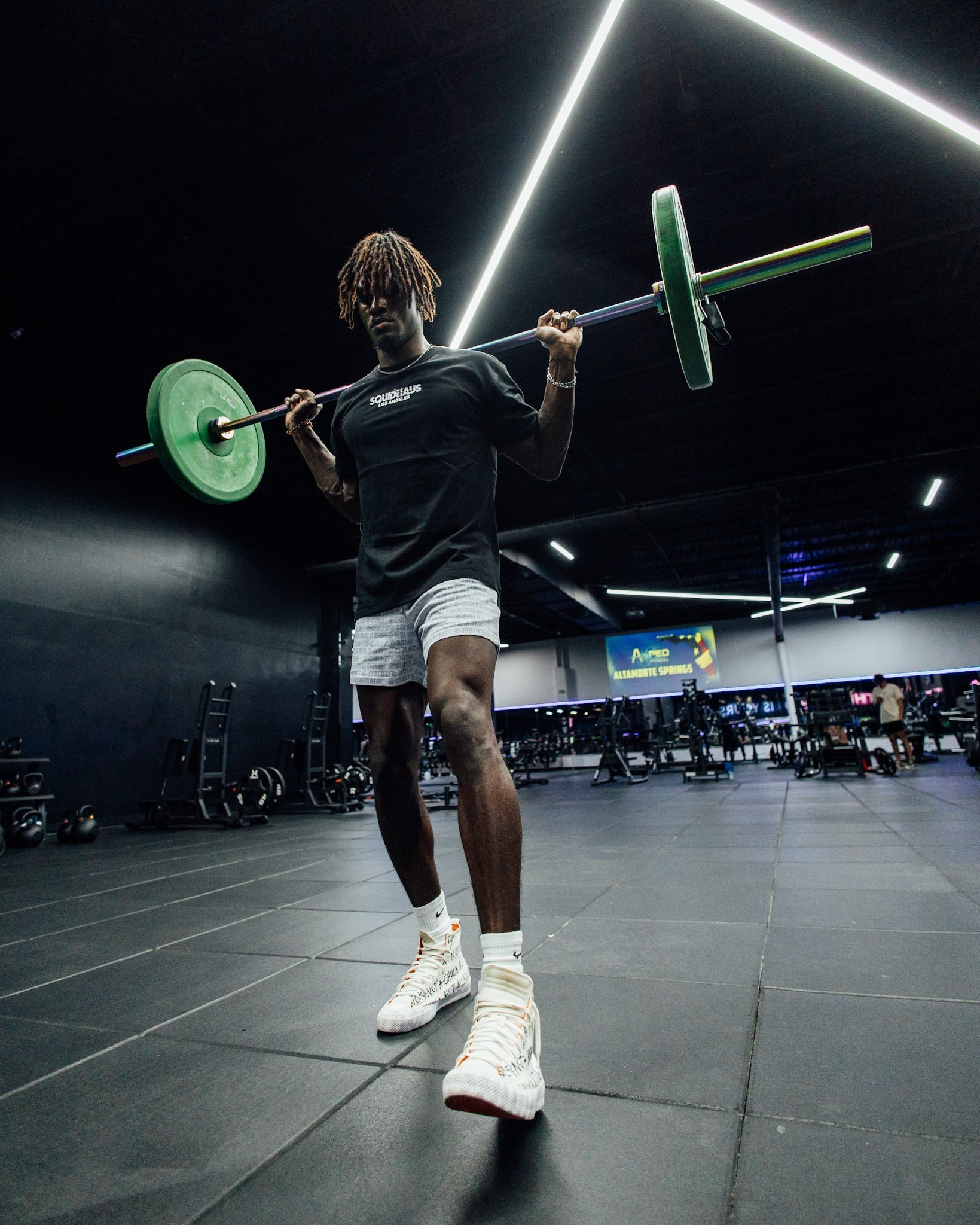 An athlete lifting weights at the gym, wearing 4 inch inseam mesh shorts in white with a long sleeve Pro-Tech V1 atheltic fitted t-shirt in black, both from SquidHaus