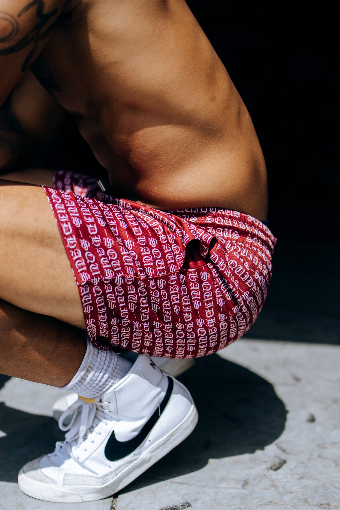 Side view of an athlete crouched down, wearing 4 inch inseam mesh shorts in red, from SquidHaus