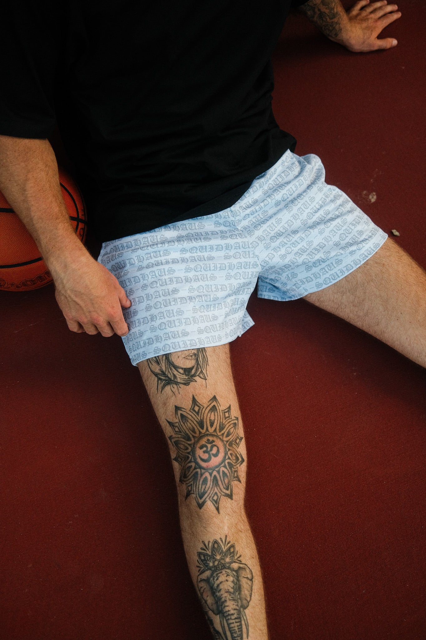 A basketball player sitting down next to a basketball while wearing 4 inch inseam mesh shorts in white, from SquidHaus