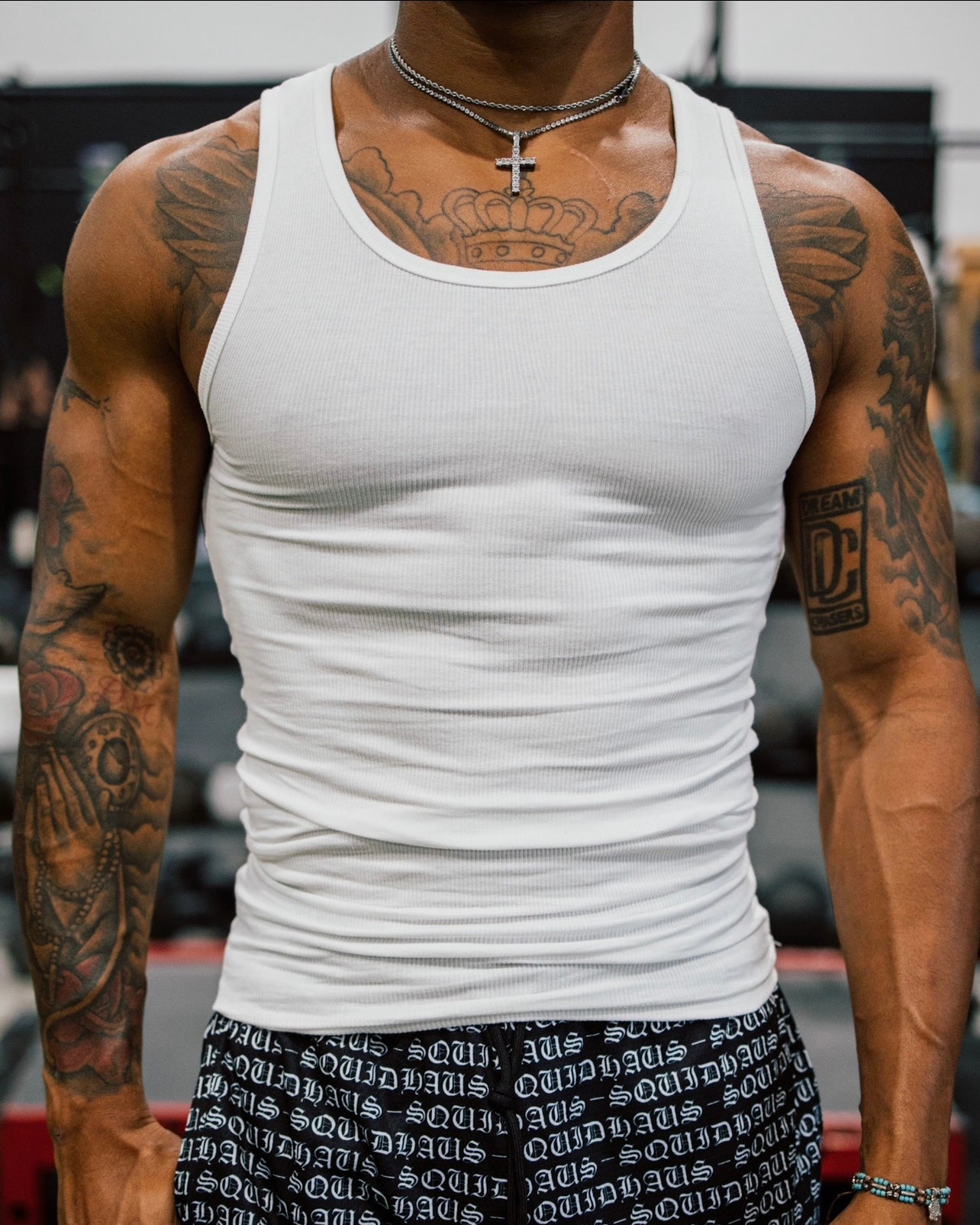 A front view of a body builder at the gym wearing 4" inseam mesh shorts in brown, and a gray athletic-fitted tank top, both from SquidHaus