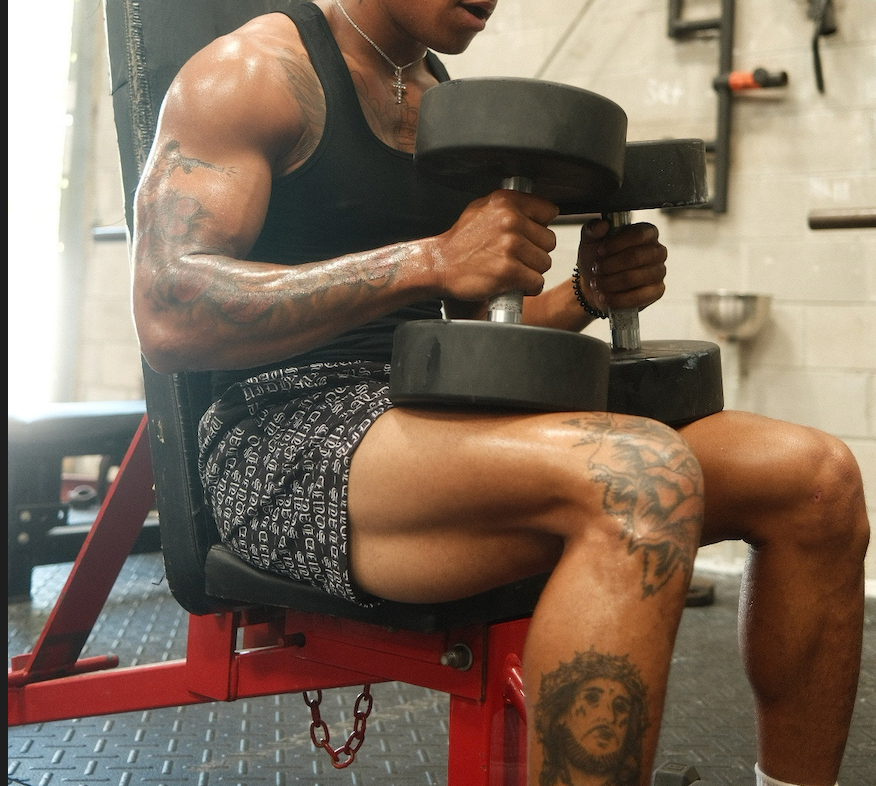 An athlete working out with large dumbells at the gym while wearing a black premium fitted workout tank top and black 4" inseam mesh shorts from SquidHaus